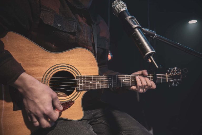 Close up a man plays an acoustic guitar in a dark room